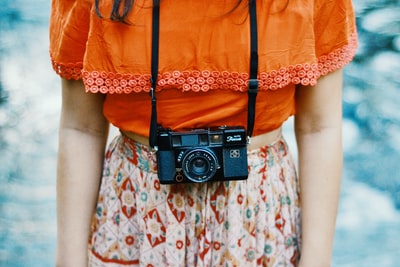 女人穿橙色和五彩缤纷的衣服黑色的桥相机在她脖子上
